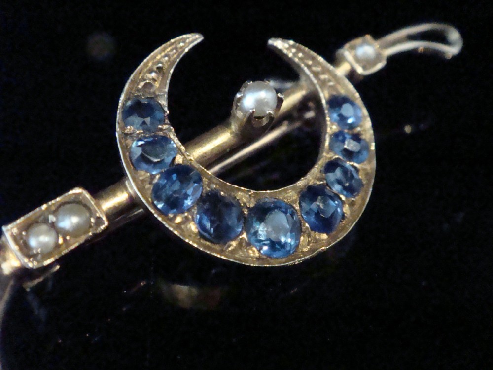 An Edwardian 9ct yellow gold bar brooch featuring a crescent moon motif set with blue sapphires and accented with seed pearls. View III