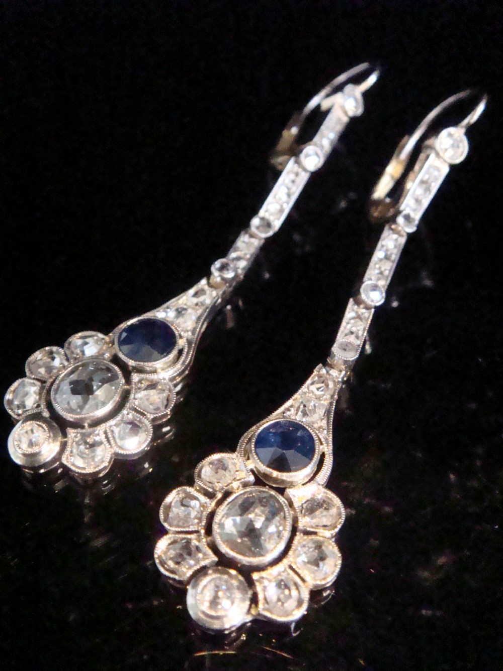 A pair of Edwardian drop earrings set in platinum featuring blue sapphires and old cut diamond floral clusters.