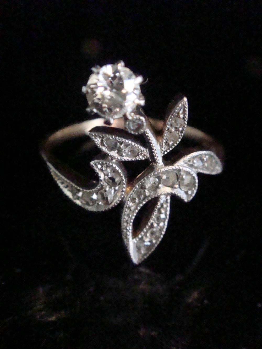 An Edwardian floral-shaped ring crafted in yellow gold and platinum, set with a central old cut diamond surrounded by diamond-encrusted leaf motifs.