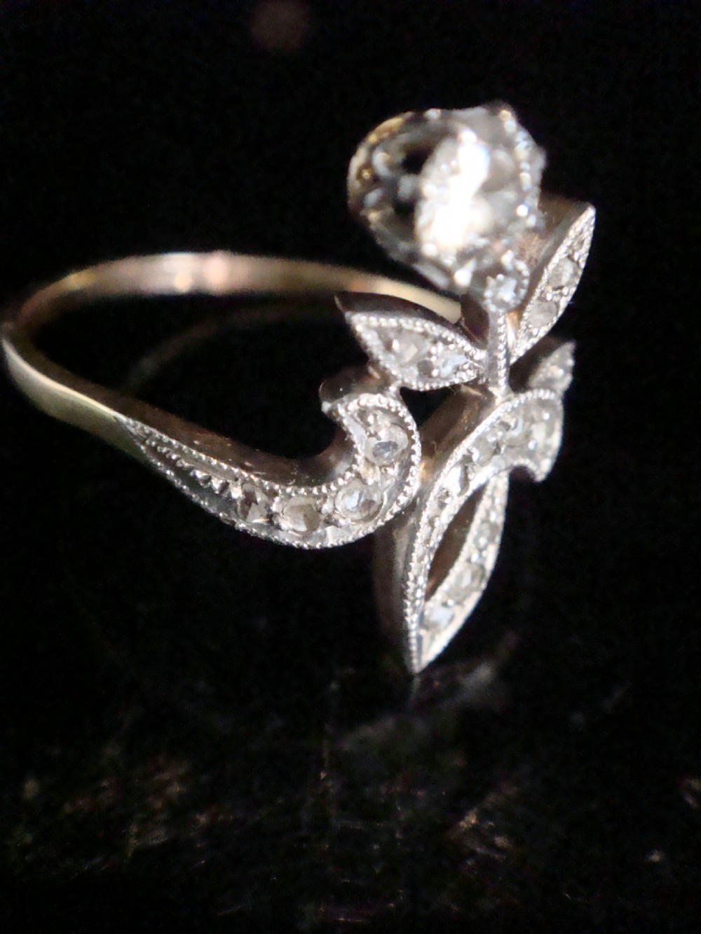 An Edwardian floral-shaped ring crafted in yellow gold and platinum, set with a central old cut diamond surrounded by diamond-encrusted leaf motifs. View V