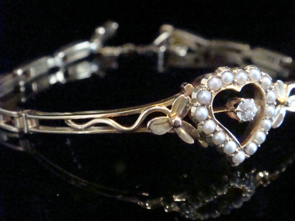 An Edwardian 9ct yellow gold bracelet featuring a central openwork heart set with seed pearls and a single diamond, flanked by sculpted foliage and wavy shoulders. View III
