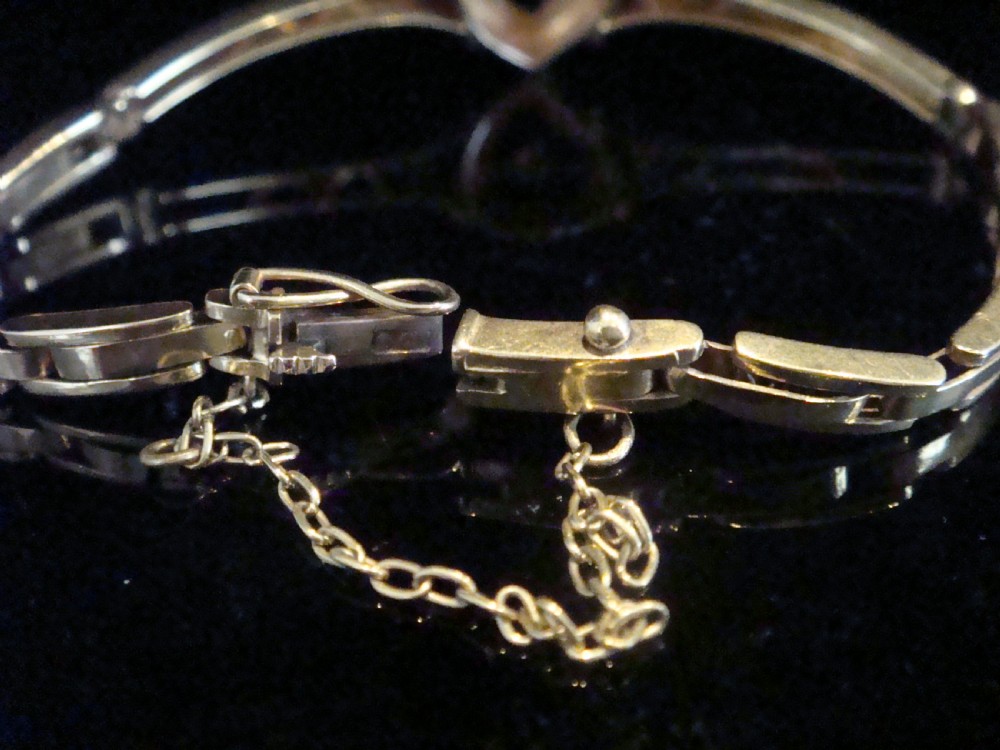 An Edwardian 9ct yellow gold bracelet featuring a central openwork heart set with seed pearls and a single diamond, flanked by sculpted foliage and wavy shoulders. View IV