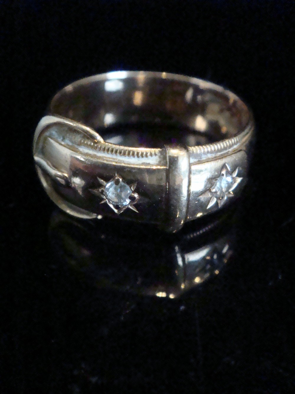 An 18ct yellow gold buckle ring with starburst-set diamonds along the strap.