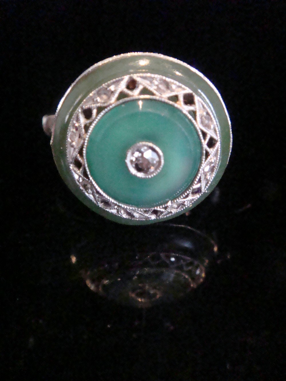 Circular Art Deco platinum target ring featuring a central old cut diamond surrounded by green chalcedony and milgrain pierced detailing.