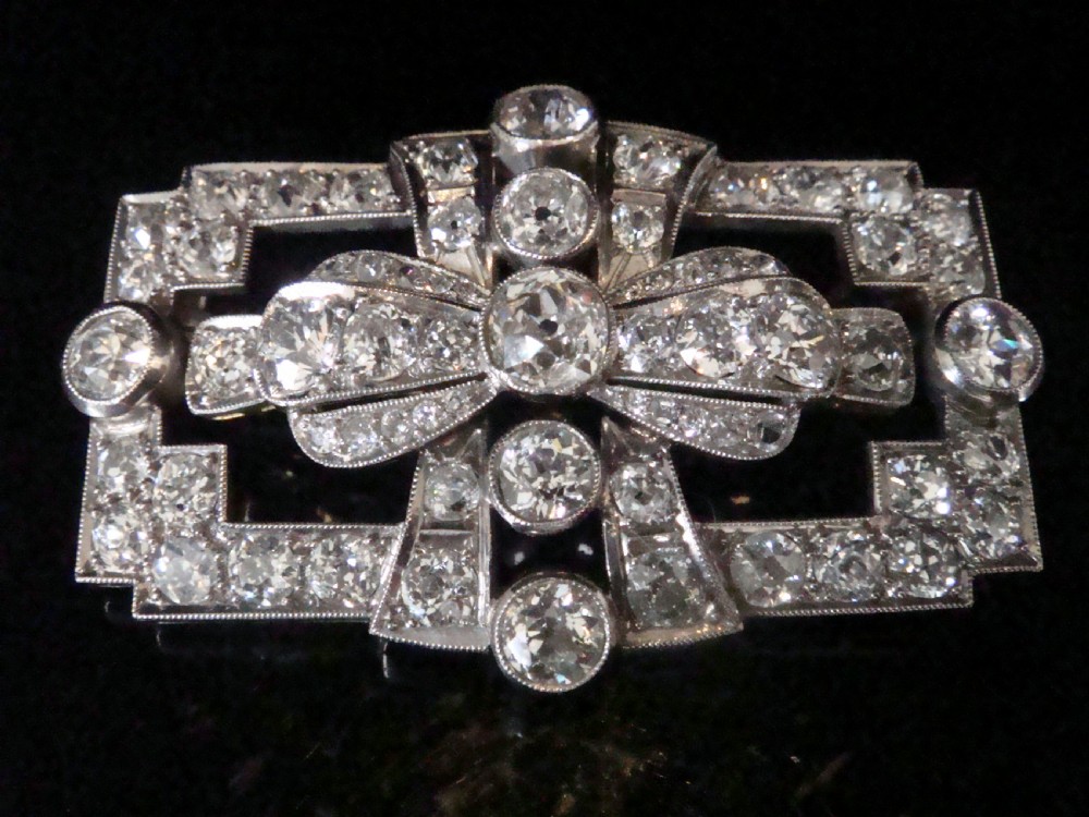 An Art Deco platinum brooch set with old cut diamonds featuring a central bow motif within a rectangular geometric frame.