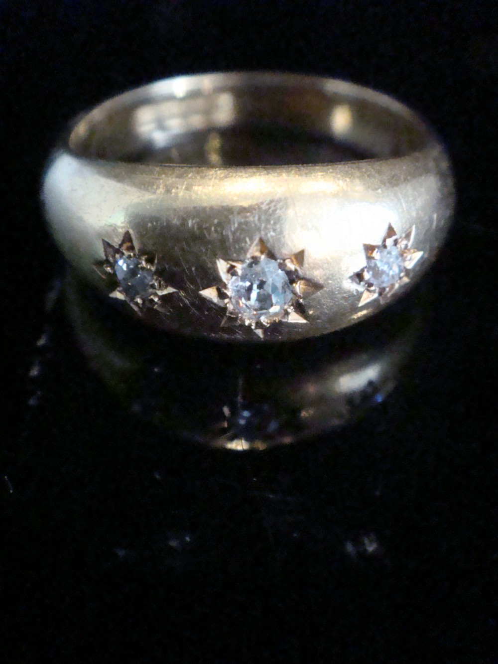 An Edwardian 18ct yellow gold band featuring three old-cut diamonds flush-set within starburst shape engravings.
