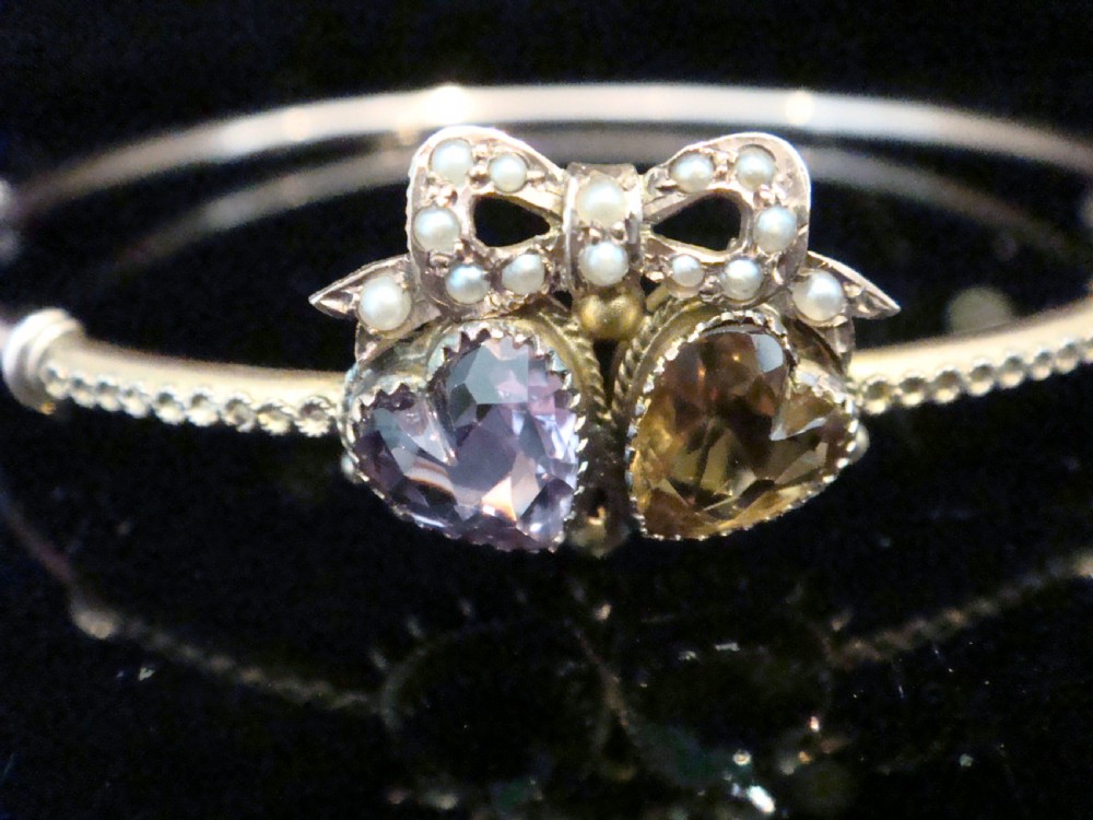 A gold hinged bangle featuring two heart-cut gemstones in purple amethyst and yellow citrine, surmounted by a bow set with small seed pearls. View II