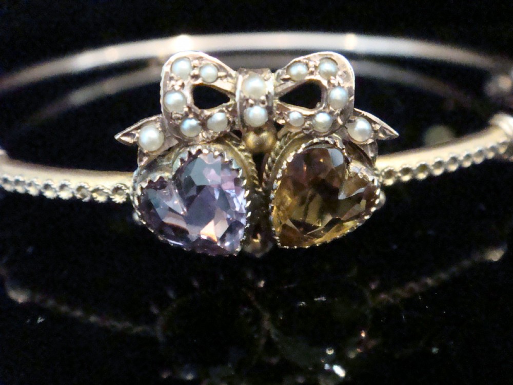 A gold hinged bangle featuring two heart-cut gemstones in purple amethyst and yellow citrine, surmounted by a bow set with small seed pearls. View III
