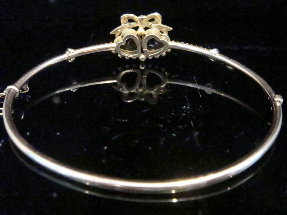 A gold hinged bangle featuring two heart-cut gemstones in purple amethyst and yellow citrine, surmounted by a bow set with small seed pearls. View IV