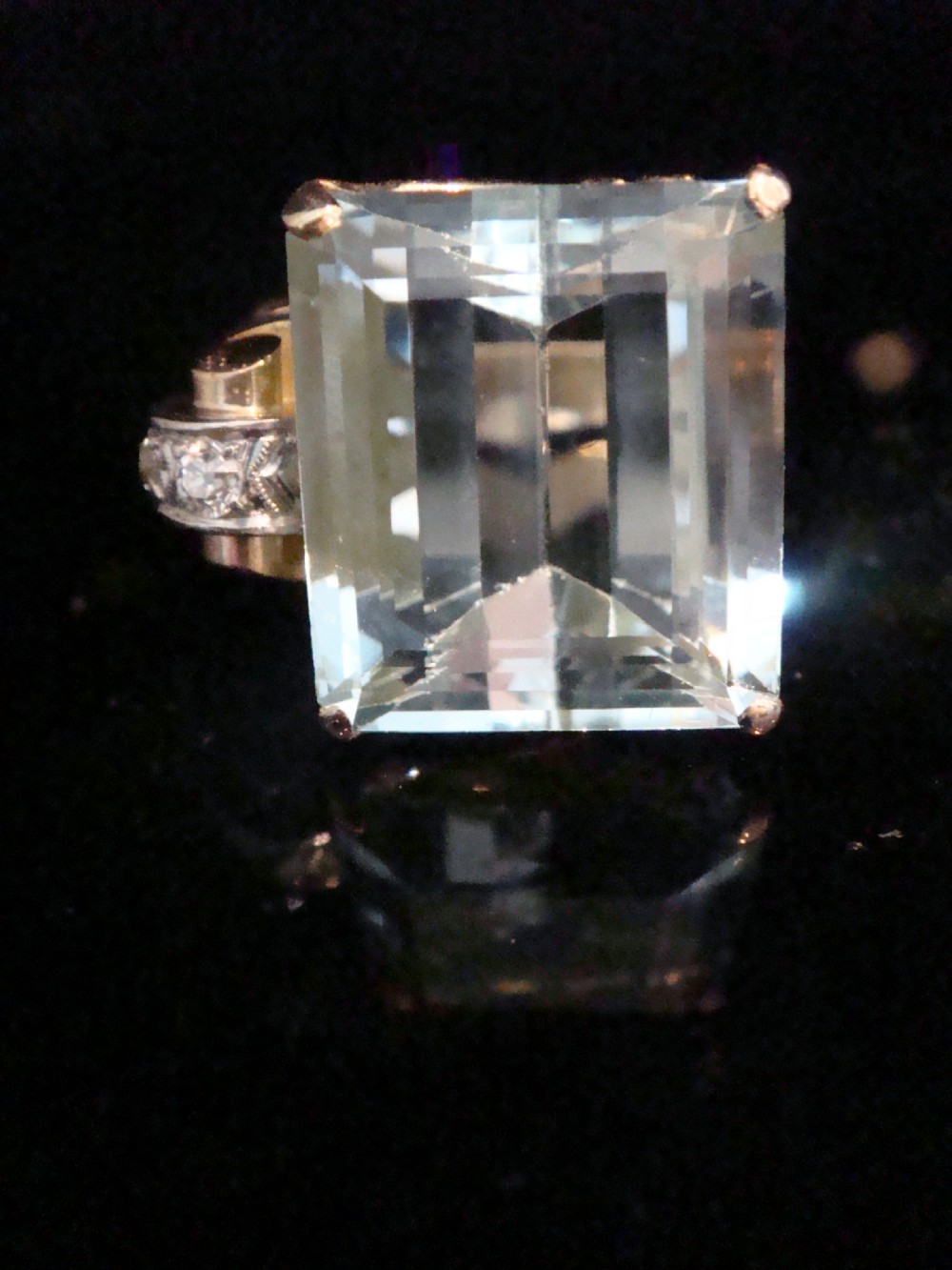 A Retro 18ct gold cocktail ring featuring a large rectangular step-cut pale blue aquamarine flanked by diamond-set tank shoulders.
