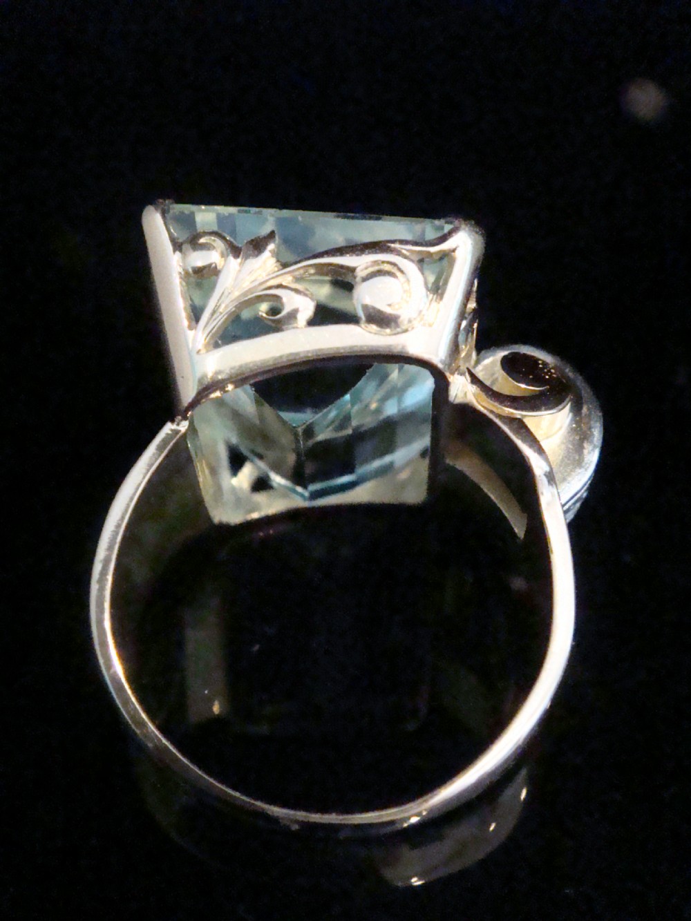 A Retro 18ct gold cocktail ring featuring a large rectangular step-cut pale blue aquamarine flanked by diamond-set tank shoulders. View IV