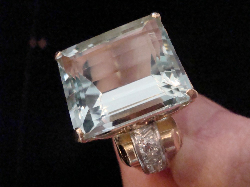 A Retro 18ct gold cocktail ring featuring a large rectangular step-cut pale blue aquamarine flanked by diamond-set tank shoulders. View VI