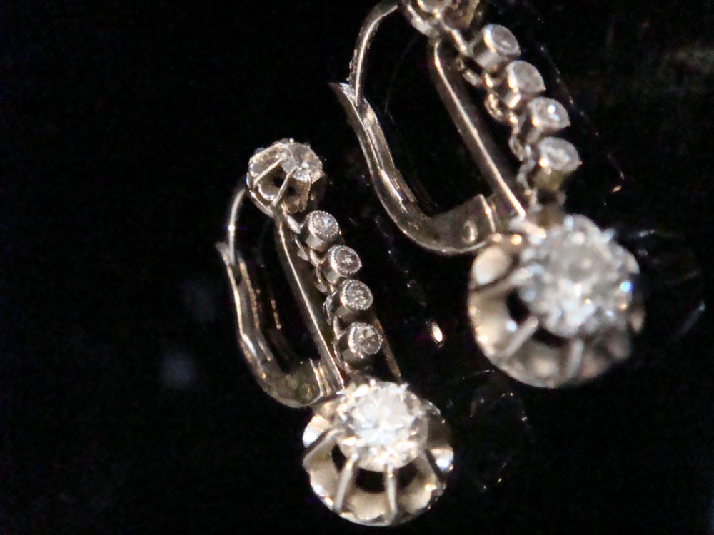 A pair of French Edwardian platinum and diamond drop earrings featuring transitional cut diamonds suspended in articulated settings.