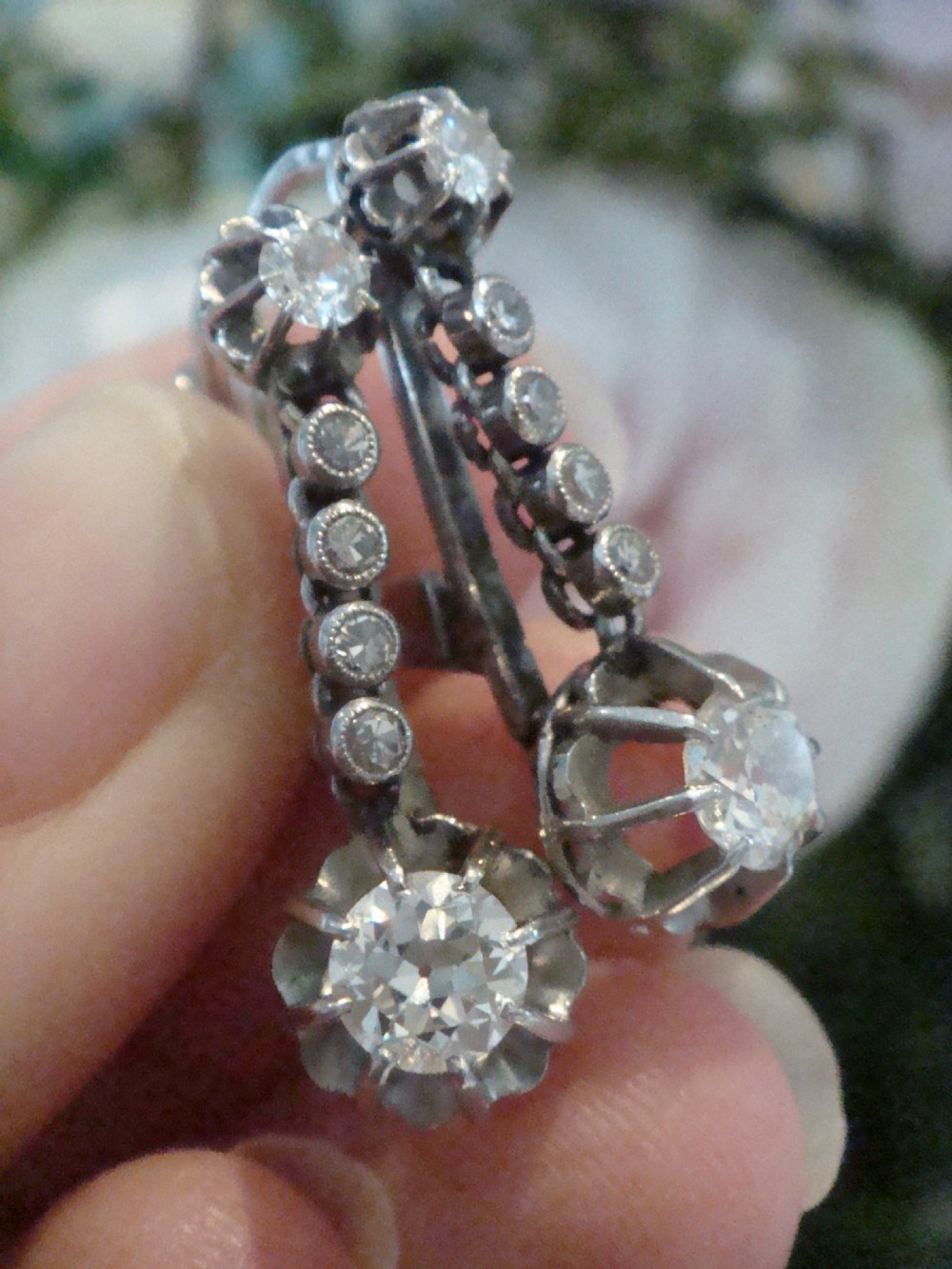 A pair of French Edwardian platinum and diamond drop earrings featuring transitional cut diamonds suspended in articulated settings. View IV