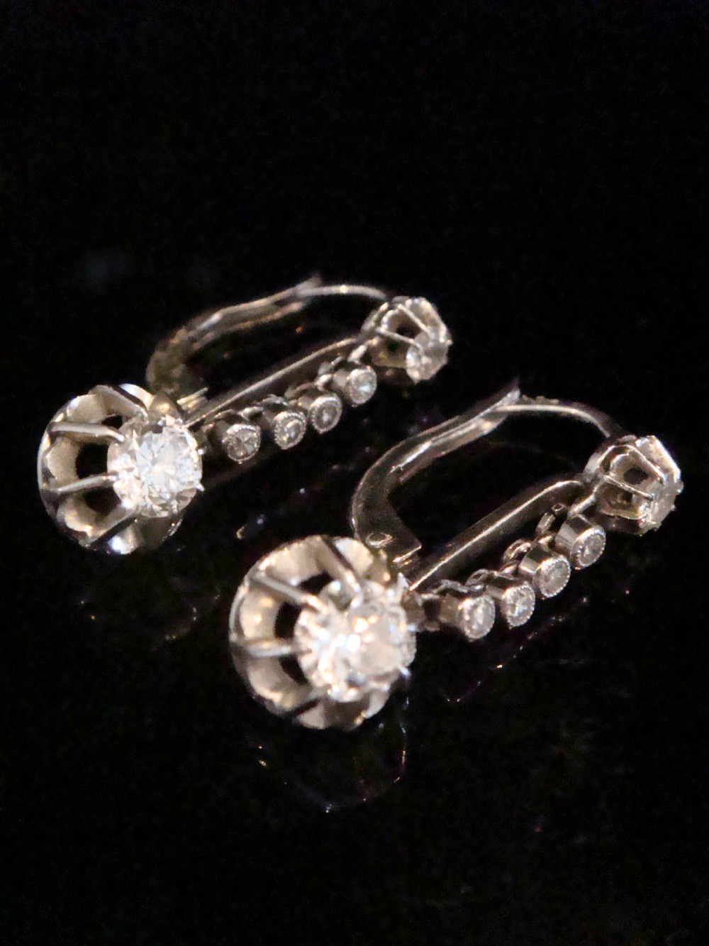 A pair of French Edwardian platinum and diamond drop earrings featuring transitional cut diamonds suspended in articulated settings. View V