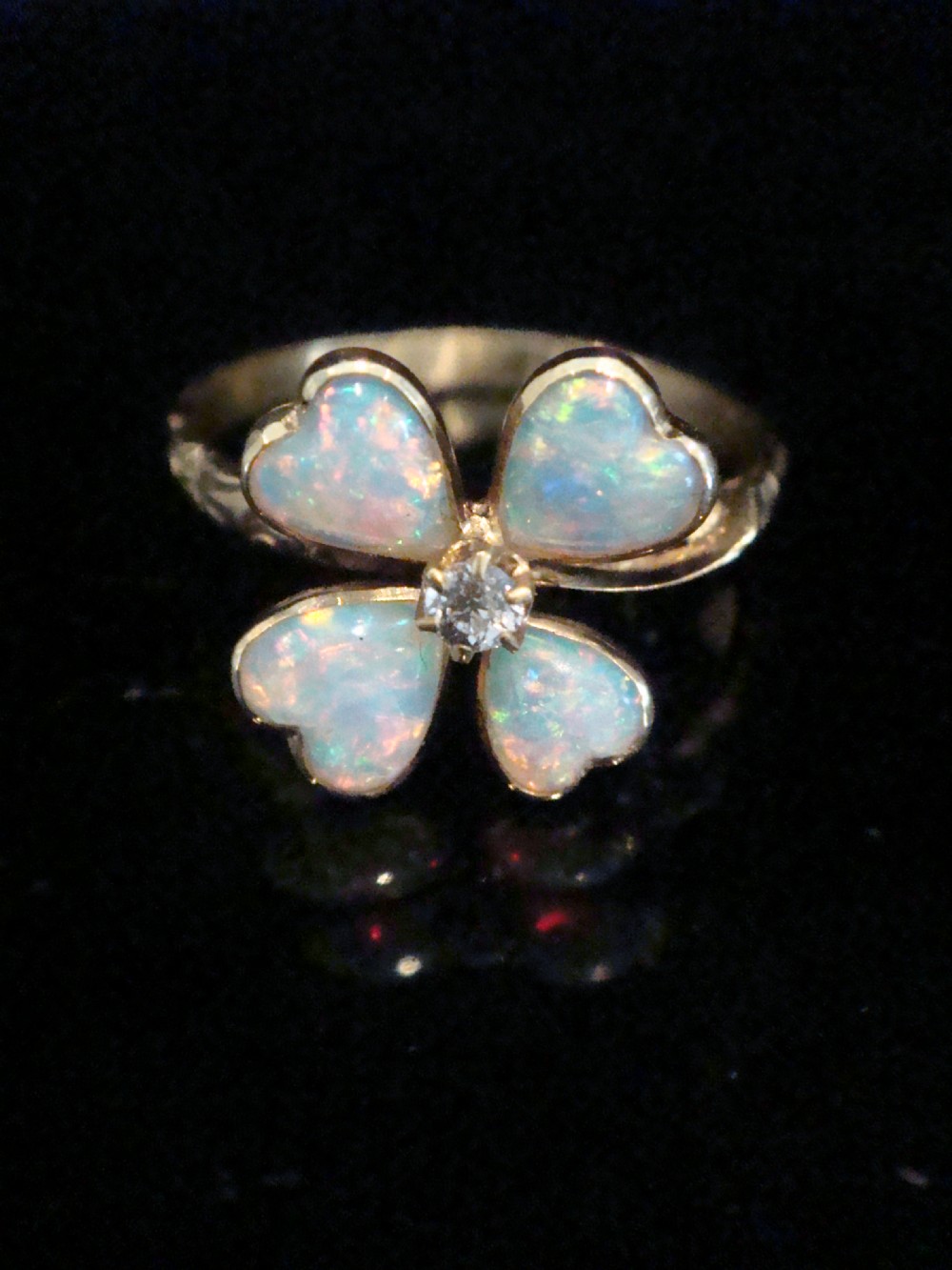 An Edwardian 18ct yellow gold ring featuring a four-leaf clover design composed of four heart-shaped opals surrounding a central round diamond.