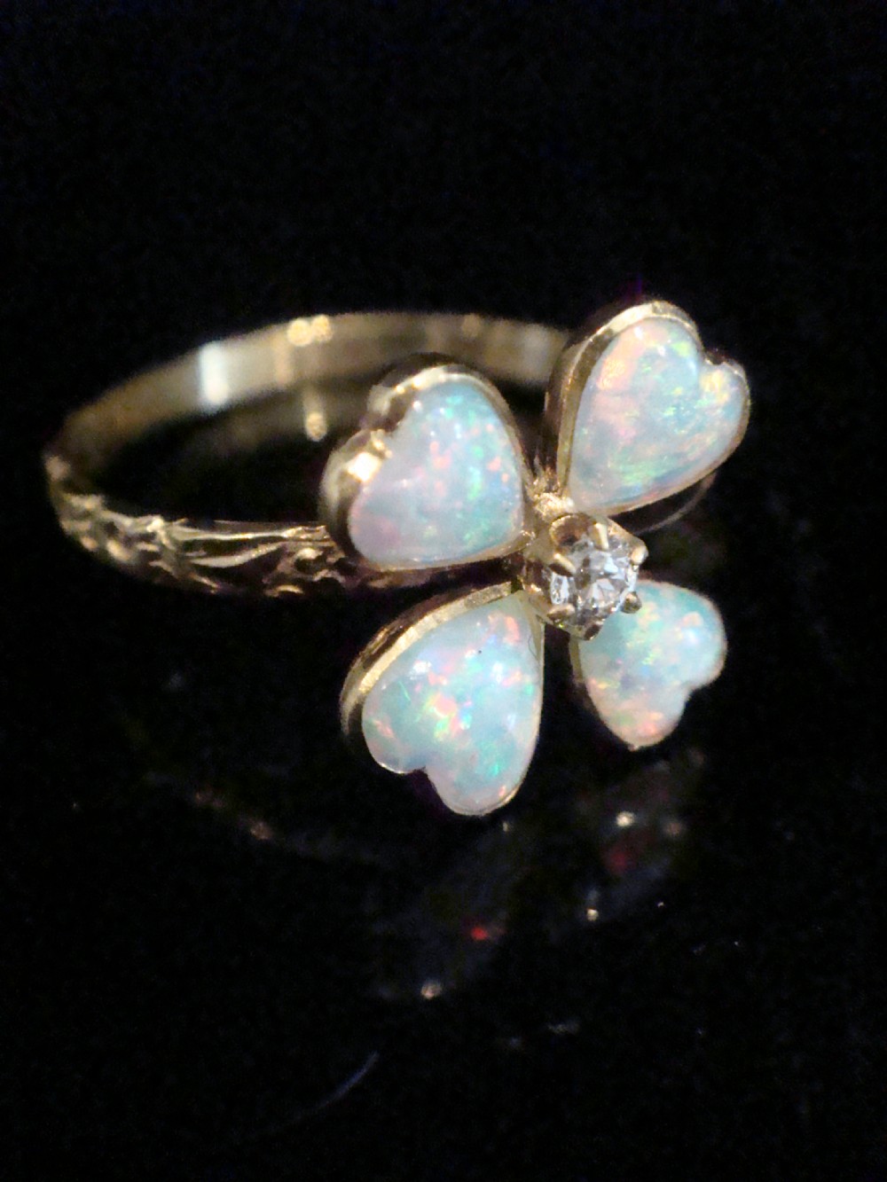 An Edwardian 18ct yellow gold ring featuring a four-leaf clover design composed of four heart-shaped opals surrounding a central round diamond. View II