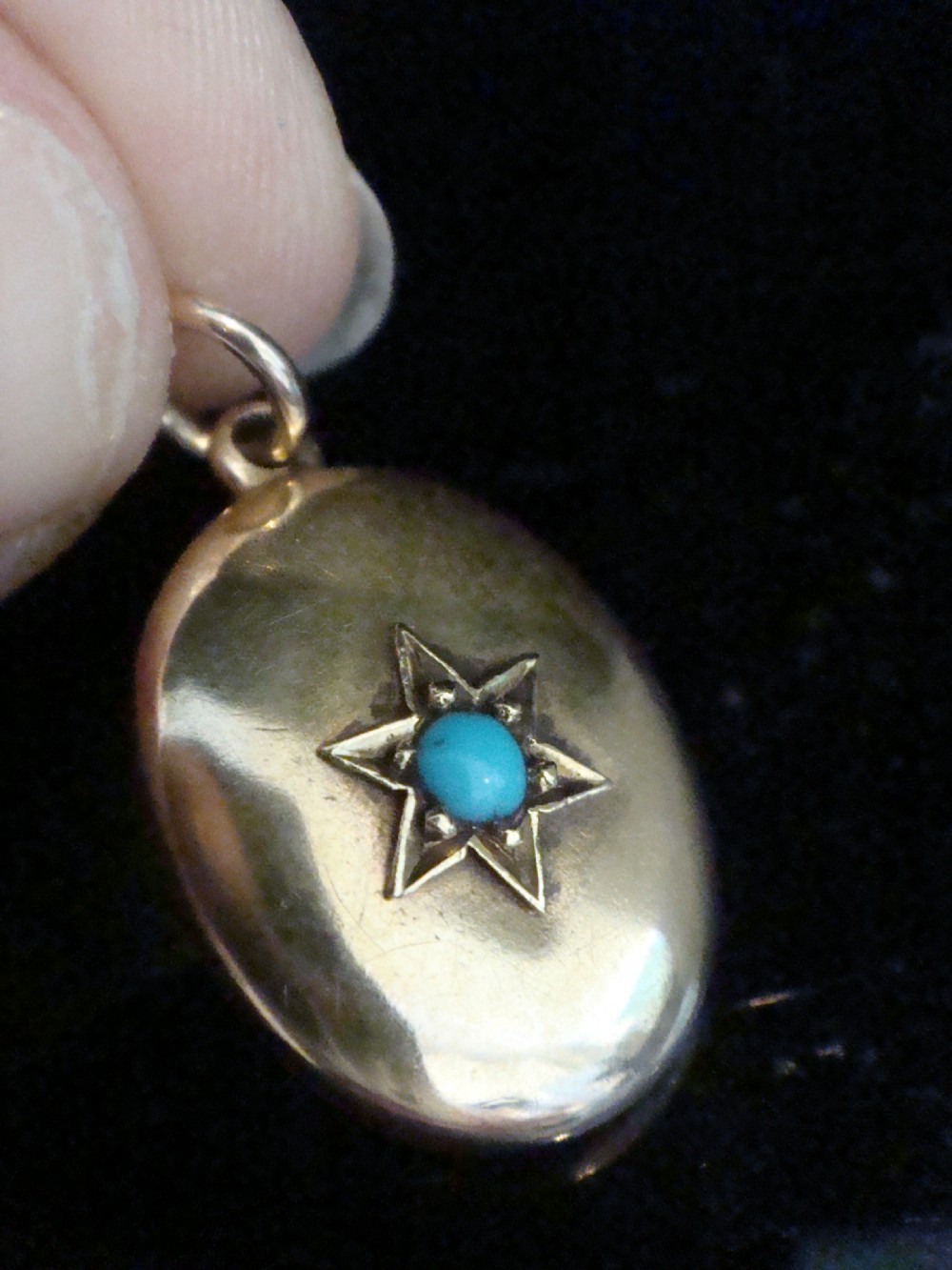 An oval 15ct yellow gold locket featuring an engraved star setting inset with a round turquoise cabochon.
