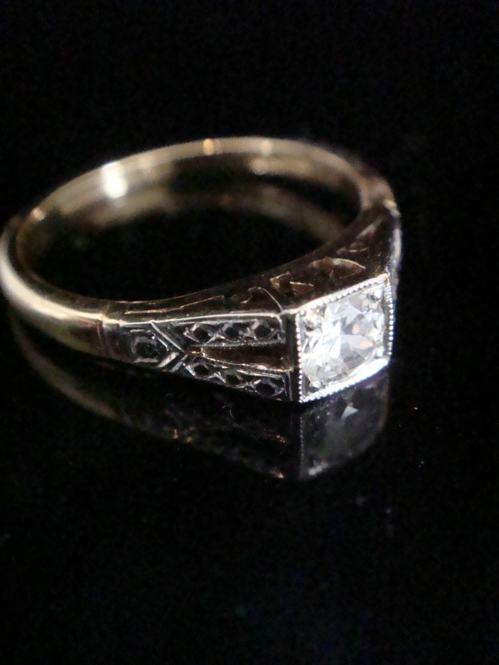 An Edwardian solitaire ring crafted in platinum and gold featuring a central old cut diamond within a square millegrain border and decorated shoulders. View II