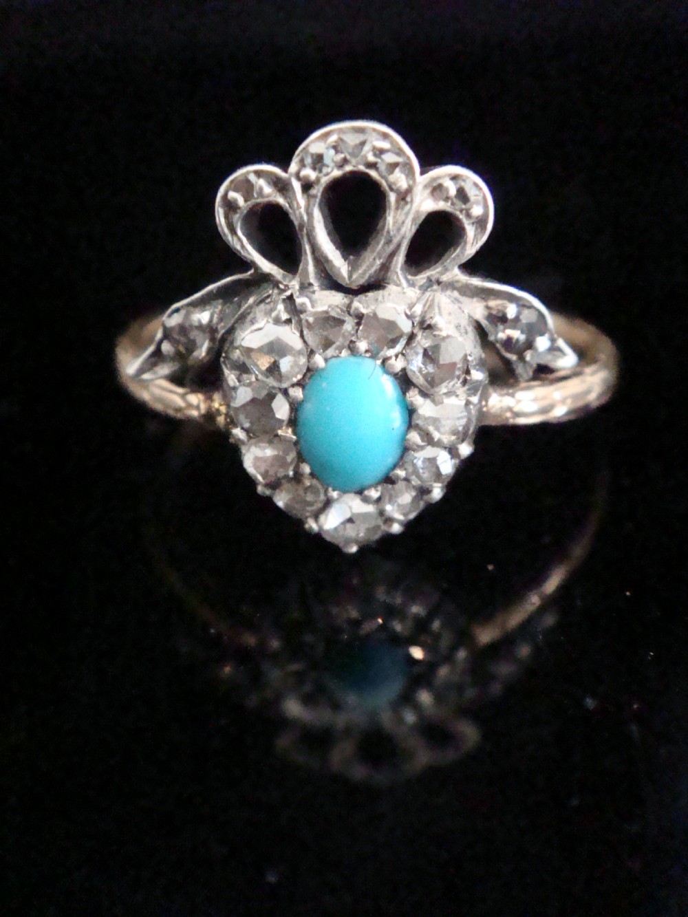 An antique heart-shaped ring featuring a central turquoise cabochon framed by rose-cut diamonds and topped with a diamond ribbon bow motif on a thin gold band.