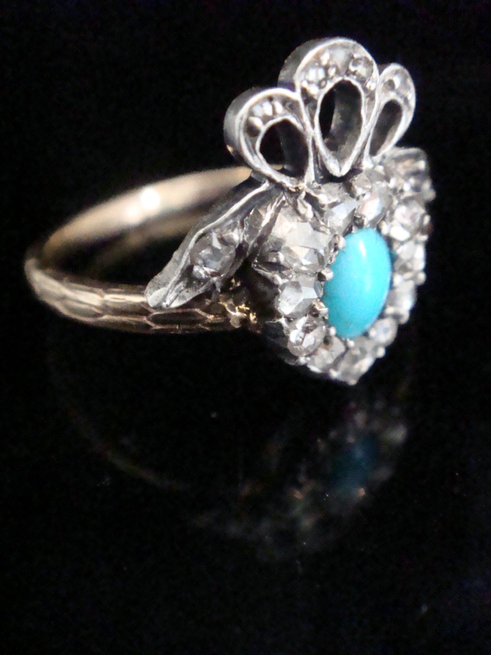 An antique heart-shaped ring featuring a central turquoise cabochon framed by rose-cut diamonds and topped with a diamond ribbon bow motif on a thin gold band. View II