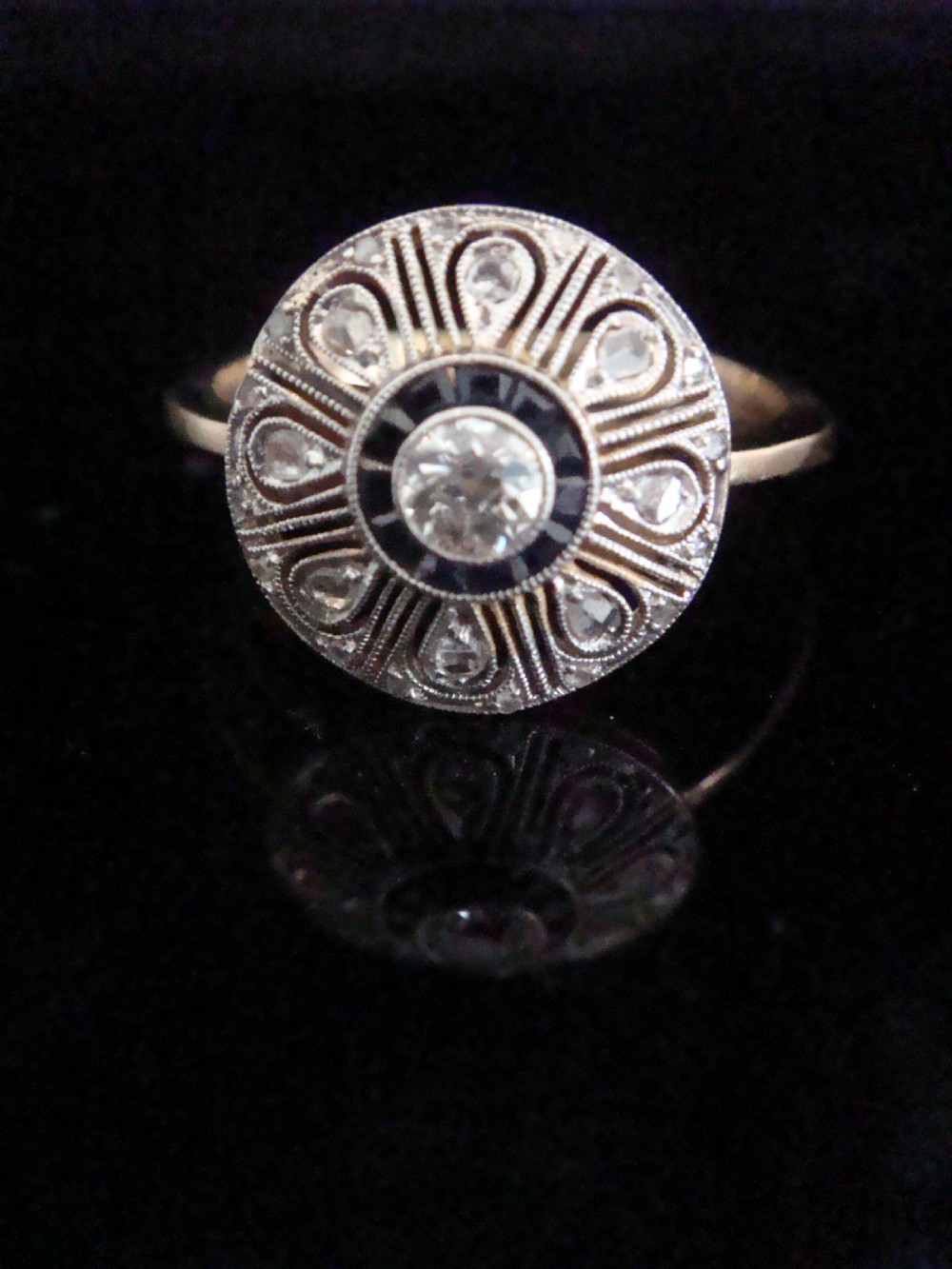 An Art Deco round target ring featuring a central diamond encircled by calibre-cut sapphires and radiating openwork set with rose-cut diamonds.