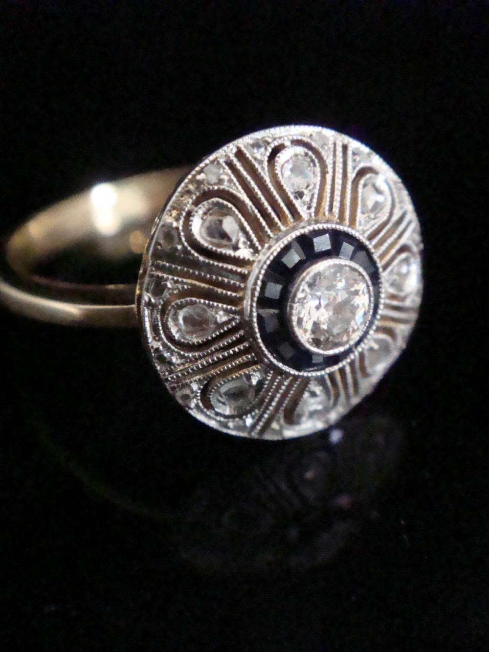An Art Deco round target ring featuring a central diamond encircled by calibre-cut sapphires and radiating openwork set with rose-cut diamonds. View III
