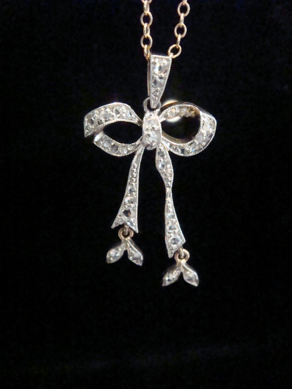 An Edwardian platinum and diamond ribbon bow pendant suspended from a fine chain.