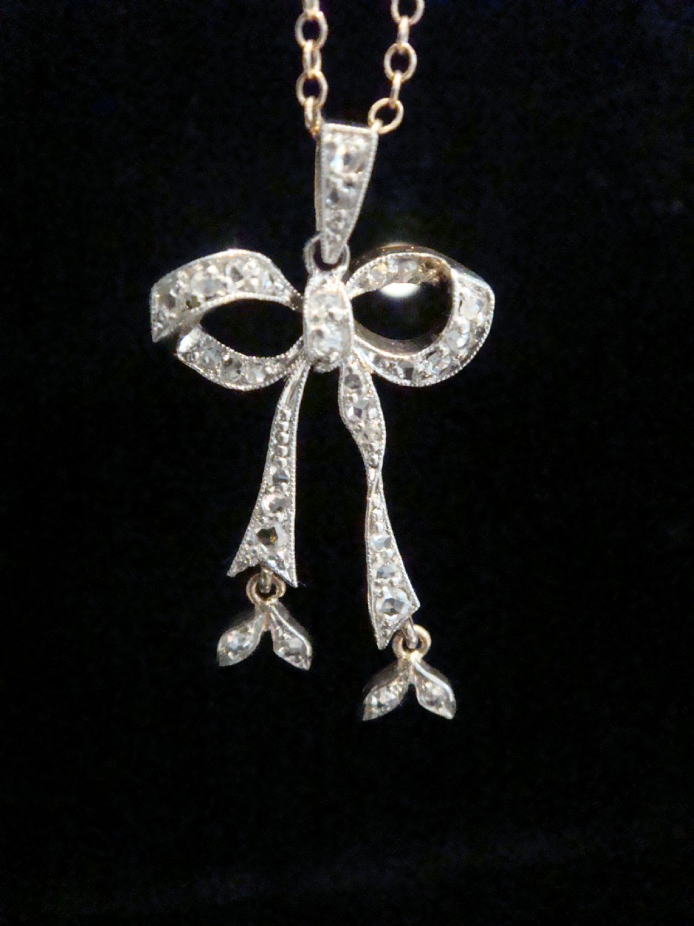 An Edwardian platinum and diamond ribbon bow pendant suspended from a fine chain. View II