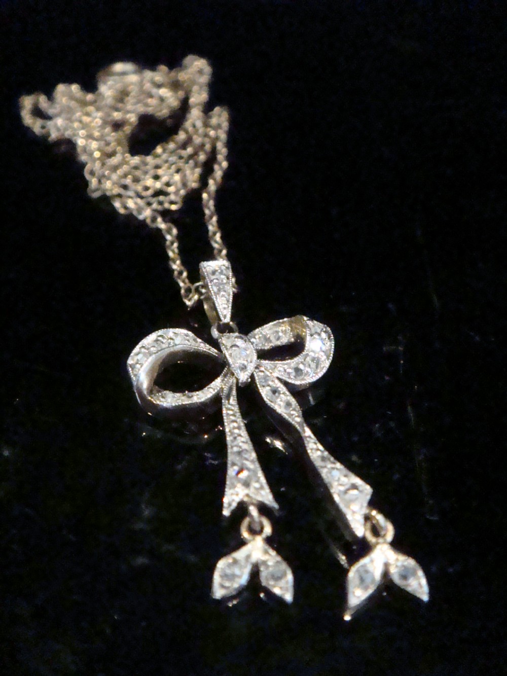 An Edwardian platinum and diamond ribbon bow pendant suspended from a fine chain. View III