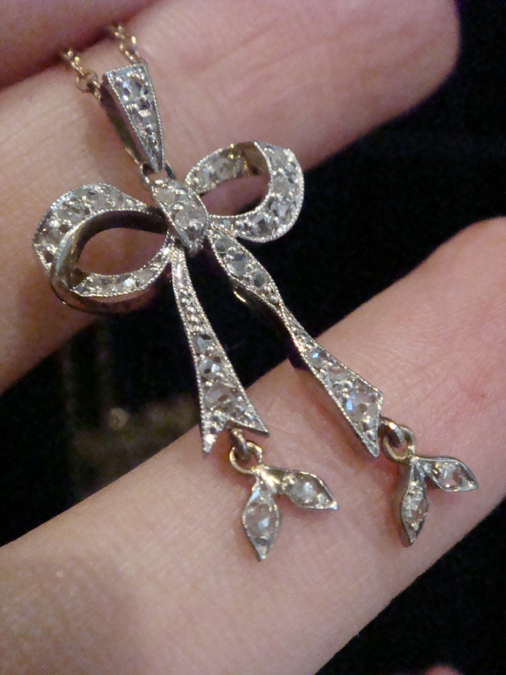An Edwardian platinum and diamond ribbon bow pendant suspended from a fine chain. View IV