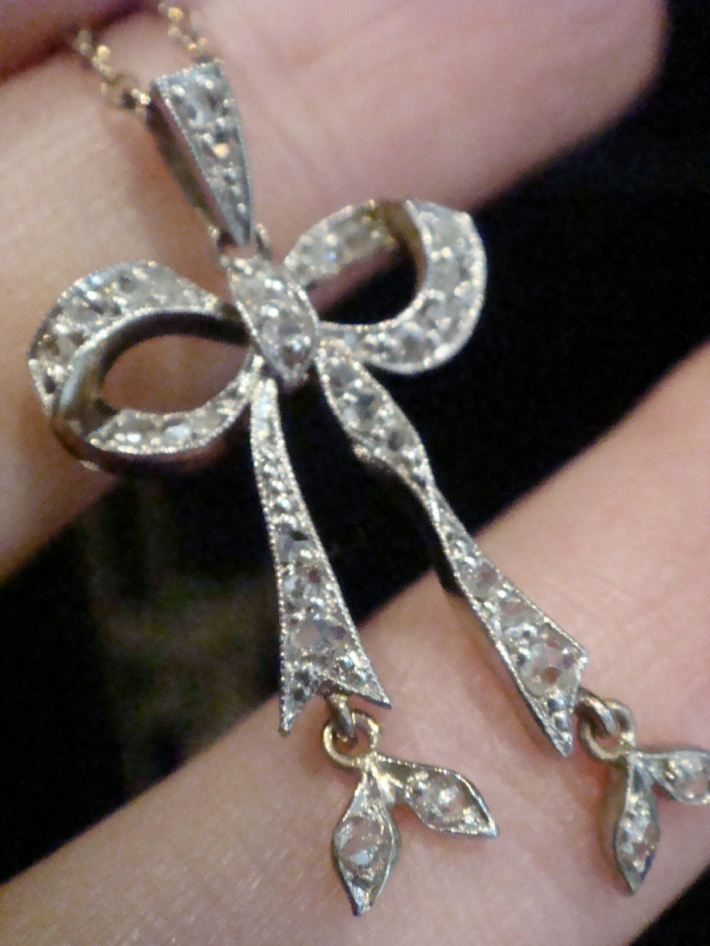 An Edwardian platinum and diamond ribbon bow pendant suspended from a fine chain. View V