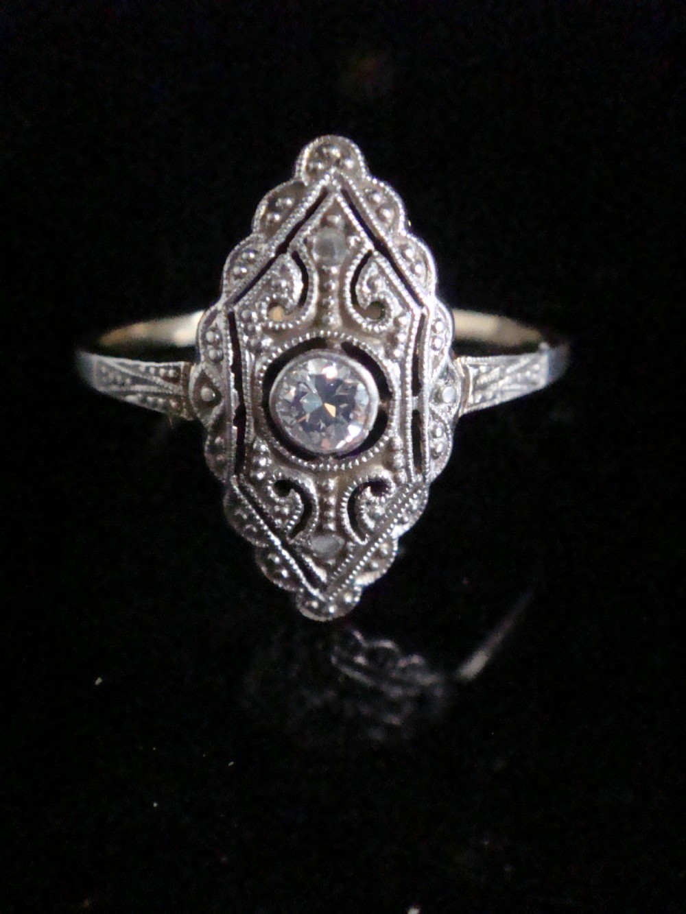 An Art Deco diamond ring featuring an elongated geometric navette setting with intricate filigree work, milgrain detailing, and a central transitional cut diamond.