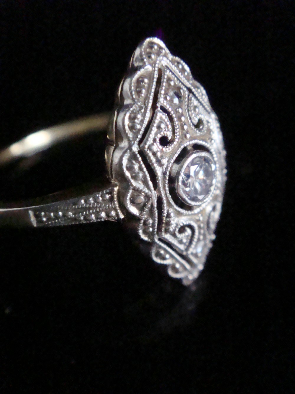 An Art Deco diamond ring featuring an elongated geometric navette setting with intricate filigree work, milgrain detailing, and a central transitional cut diamond. View II