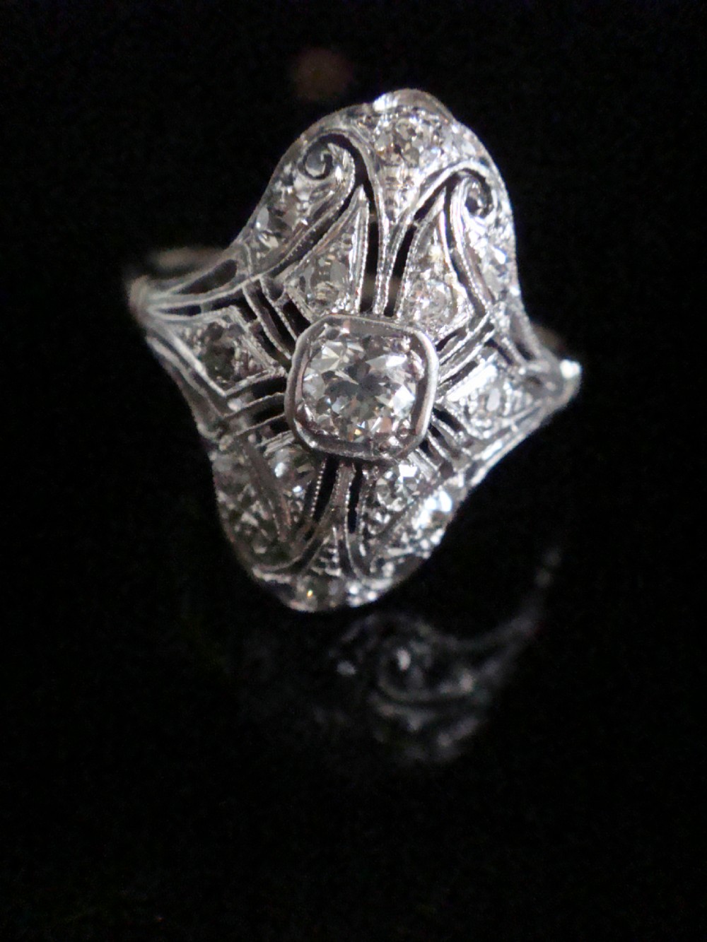 An Art Deco platinum ring featuring a central transitional-cut diamond surrounded by intricate openwork filigree set with accent diamonds. View V