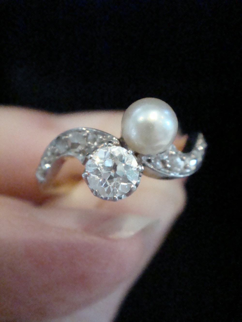 An Edwardian French 18ct yellow gold toi et moi ring set with a single cultured pearl and an old-cut diamond on a curved bypass band with accent diamonds. View V