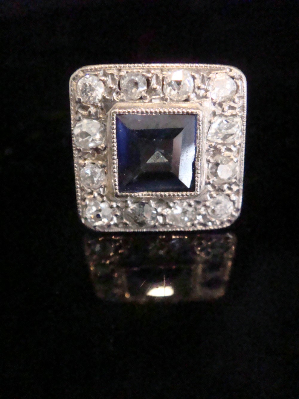 An Edwardian platinum and gold square cluster ring featuring a blue synthetic sapphire surrounded by old cut diamonds with a millegrain edge. View III