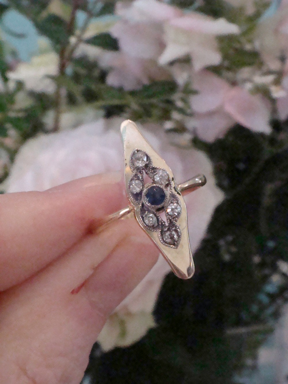 An Edwardian marquise-shaped ring featuring a central round blue sapphire encircled by old cut diamonds set in platinum atop an 18ct yellow gold band. View II