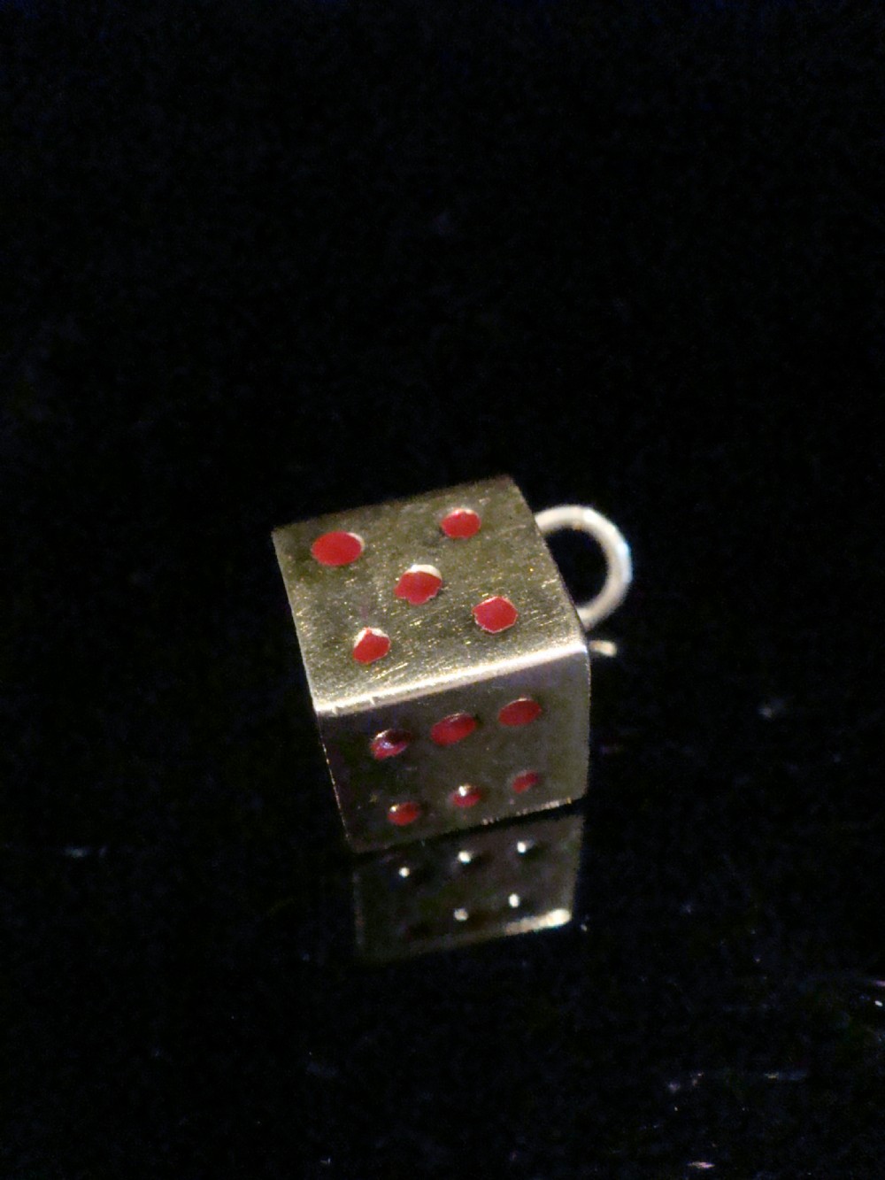 A small three-dimensional 9ct yellow gold dice pendant featuring inset red enamel pips and a top suspension ring.