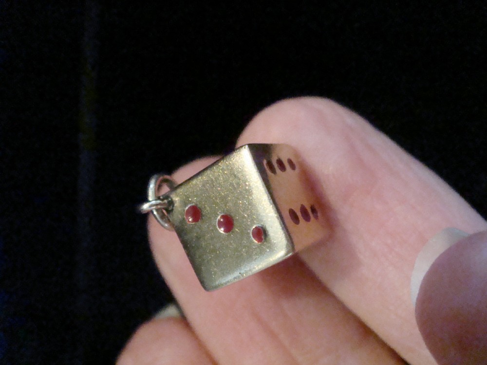 A small three-dimensional 9ct yellow gold dice pendant featuring inset red enamel pips and a top suspension ring. View II
