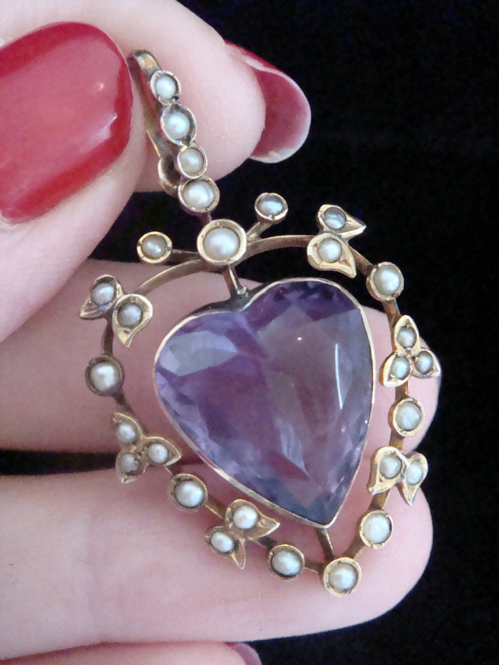 An Edwardian yellow gold heart-shaped pendant featuring a central faceted heart amethyst bordered by small seed pearls.