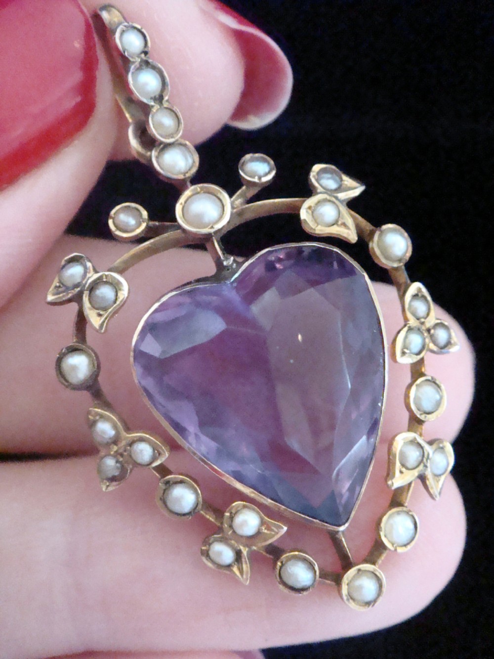An Edwardian yellow gold heart-shaped pendant featuring a central faceted heart amethyst bordered by small seed pearls. View II