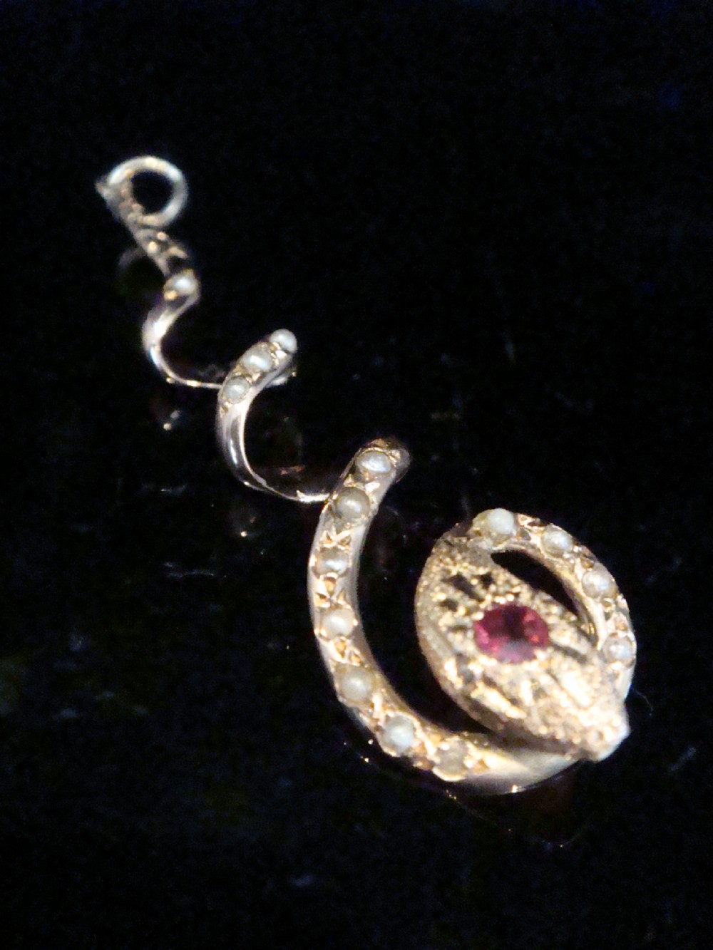 An Edwardian 9ct gold spiral snake pendant set with seed pearls along the coiled body and a red ruby accent in the head.