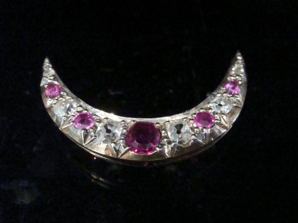 An Edwardian 18ct yellow gold crescent brooch featuring alternating natural red rubies and clear diamonds.