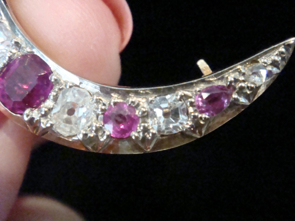 An Edwardian 18ct yellow gold crescent brooch featuring alternating natural red rubies and clear diamonds. View V