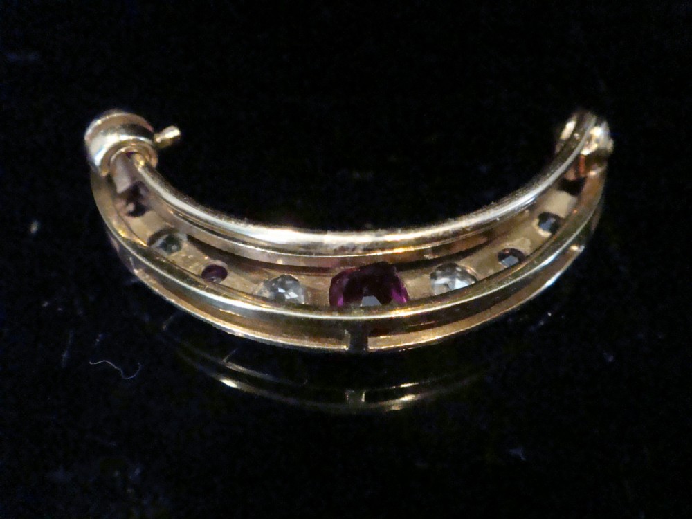 An Edwardian 18ct yellow gold crescent brooch featuring alternating natural red rubies and clear diamonds. View VII