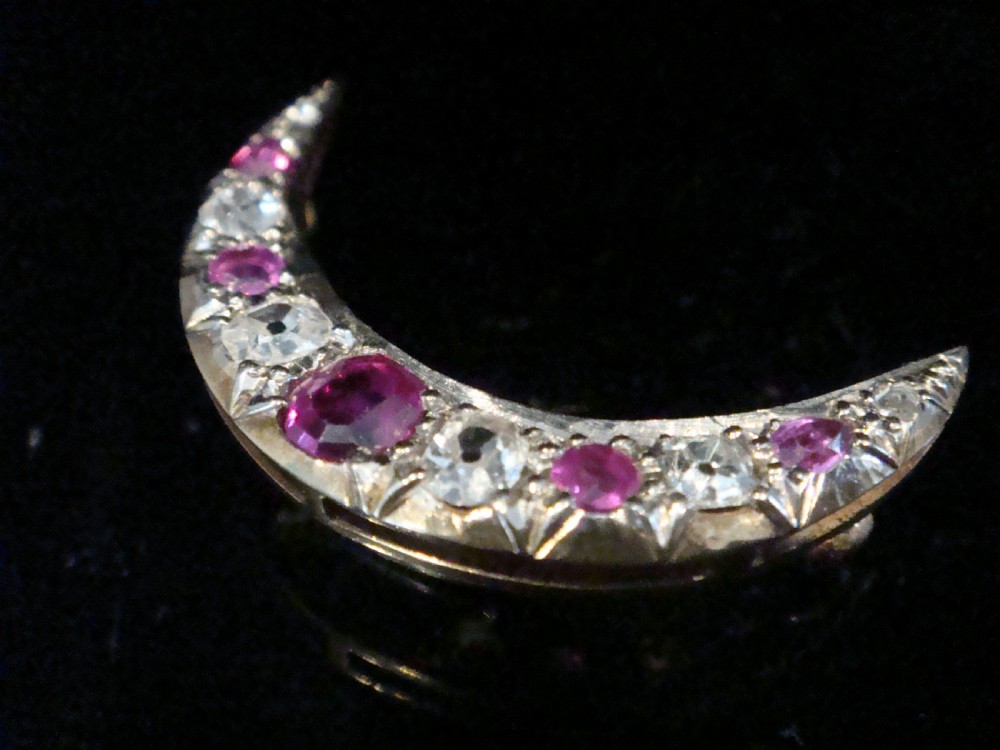 An Edwardian 18ct yellow gold crescent brooch featuring alternating natural red rubies and clear diamonds. View VIII