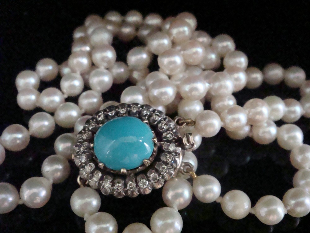 A strand of white cultured pearls fastened with an Edwardian clasp set with a central turquoise cabochon surrounded by a halo of diamonds.