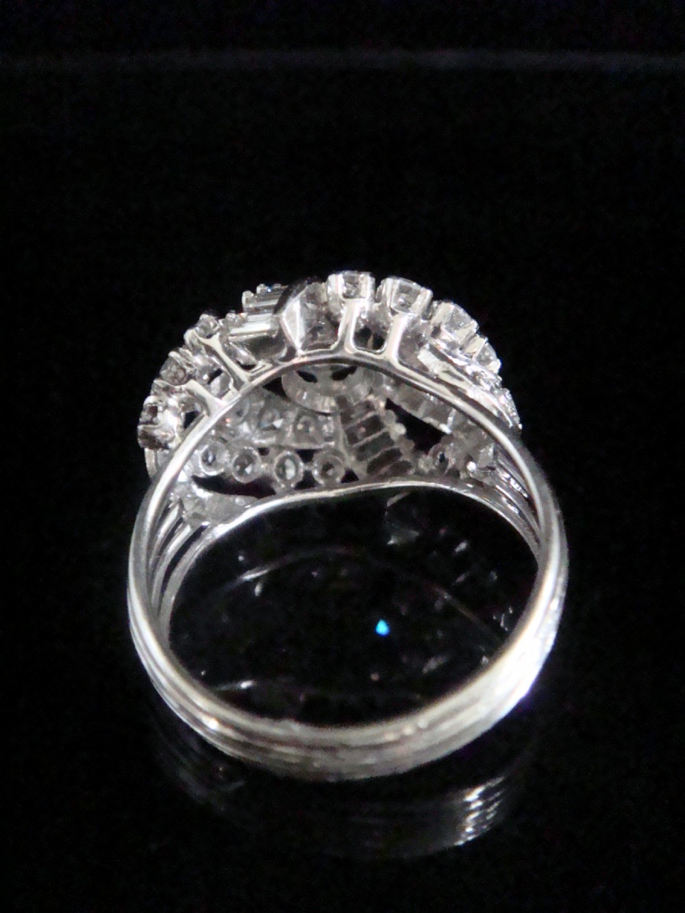 An Art Deco diamond bombe ring featuring a central transitional cut diamond surrounded by sculpted rows of round and baguette cut diamonds set in white gold. View III