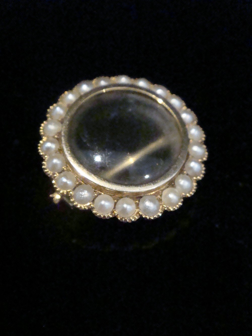 A circular Edwardian 9ct yellow gold locket brooch set with a perimeter halo of seed pearls framing a central glazed glass compartment.